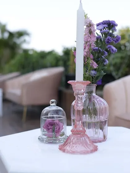 A close-up of a centerpiece from Reeya and Parth's wedding, featuring a single rose under a glass cloche and a pink candle holder.