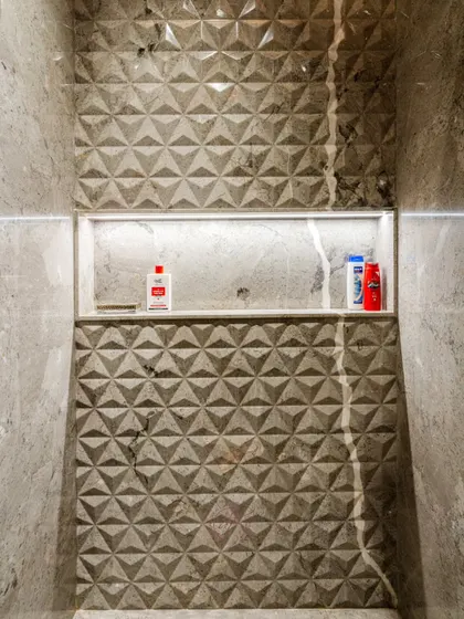 The recessed shower niche with integrated lighting is a practical and modern storage solution. The 3D geometric tiles create a beautiful, textured backdrop.