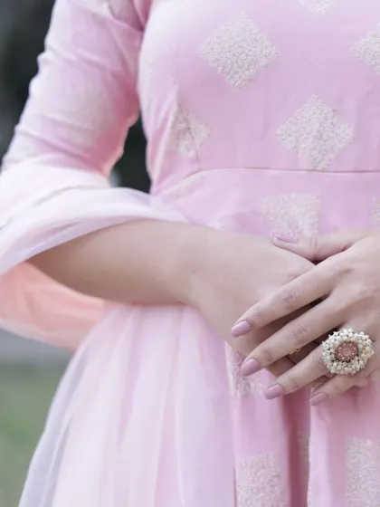 A close-up on the hands, showing off a beautiful statement ring and the delicate fabric of the pink dress. Detail shots like this are crucial for e-commerce.