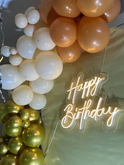 A detail shot of the 'Happy Birthday' neon sign against the balloon garland. Neon signs are a fantastic way to add a personalized and trendy element to any party.