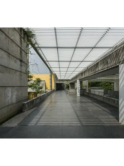 The main circulation spine of the IIM Sports Center is a pergola-covered double-height space. The play of light and shadow from the pergola creates a dynamic experience while providing a sheltered connection between facilities.