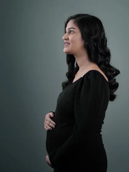 A beautiful profile shot of an expecting mother in a simple black dress. The clean studio lighting emphasizes her gentle smile and the curve of her baby bump.