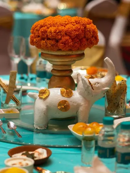 A stunning table centerpiece for a 'Sajjangoth' dinner, featuring a marigold arrangement and a small, decorative white elephant. This detail adds a playful and traditional touch to the tablescape.