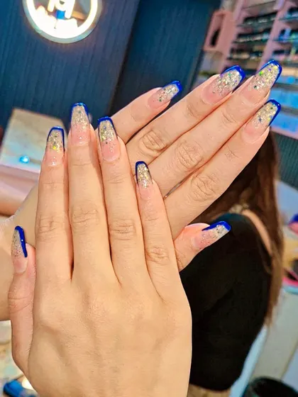 A glamorous take on the French manicure, featuring coffin-shaped nails with a deep blue tip and a cascade of gold glitter. This design is perfect for parties and festive events.