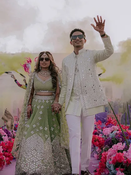 The couple makes a grand entrance through a path of flowers and colored smoke, their modern, stylish look perfect for a wedding carnival.