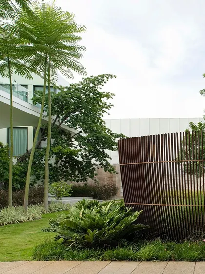 A curved Corten steel screen provides a sculptural boundary for a residential lawn. The design uses the screen to create privacy while adding an artistic element that complements the modern architecture and surrounding greenery.