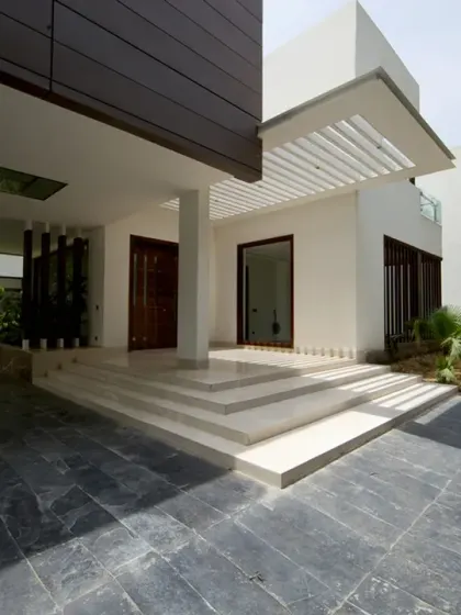 The entrance to the Sachdeva Farmhouse is marked by a cantilevered zinc-clad block, a first in India. Wide polished stone steps rise to a sheltered porch, creating a refined and modern threshold framed by lush landscaping.