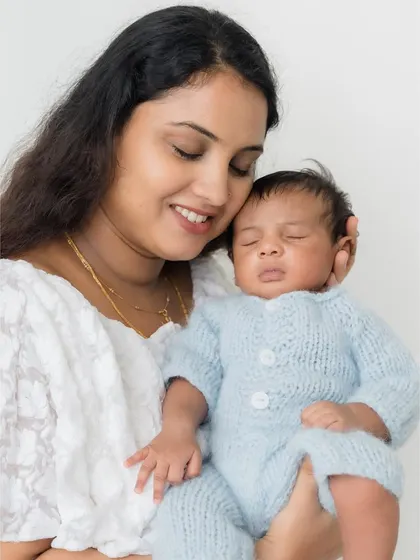 A mother gazes down at her sleeping newborn, dressed in a cozy blue knit outfit.