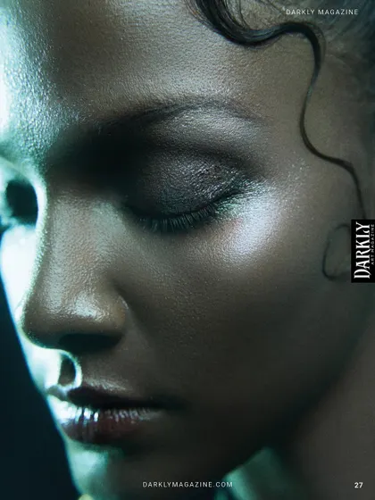 A close-up beauty shot from a Darkly Magazine editorial, focusing on glowing skin and wet-look makeup.