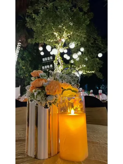 A simple yet elegant table centerpiece with a candle and flowers, set against the backdrop of trees wrapped in fairy lights. It's the small touches that create a magical ambiance.