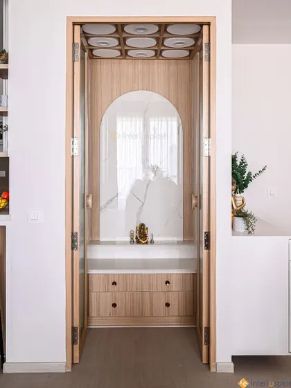 This elegant puja unit is designed with a light wood frame and a marble-patterned backdrop. The folding doors allow it to be neatly closed off when not in use.