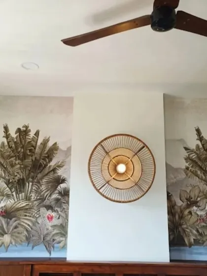 A symmetrical tropical mural frames a central wall light, creating a balanced and calming feature wall in this bedroom.