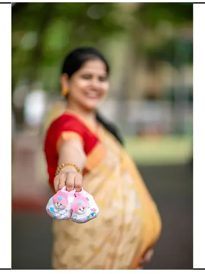 A creative shot with the focus on the baby shoes held out by the mom-to-be, who is smiling in the background.