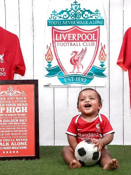A joyful shot of a little Liverpool FC fan, laughing and holding a football. We love capturing these happy moments for sports-loving families.