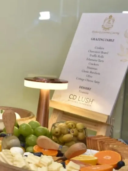 An elegant grazing board and custom menu for the CD Lush clinic launch by Clinic Dermatech. The setup includes a variety of cheeses, olives, and fruits, presented with a modern table lamp for a warm glow.