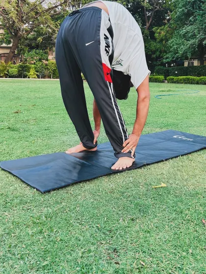A standing forward bend, or Uttanasana, demonstrated in a park. This pose is great for calming the mind and stretching the hamstrings.