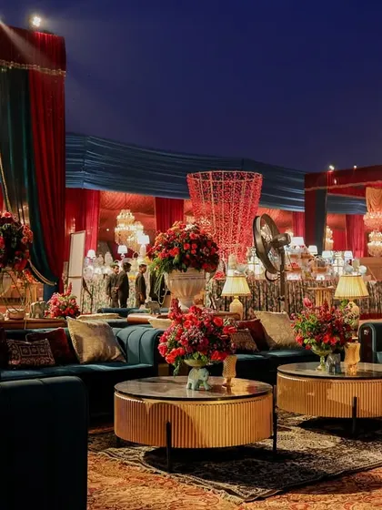 An evening view of the lounge area, where deep teal sofas are set against a backdrop of red and gold drapery. The lighting creates a warm, inviting ambiance for guests to relax and socialize.