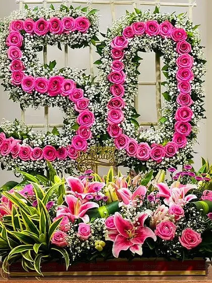 A magnificent floral arrangement celebrating a 50th birthday. We created the number "50" using bright pink roses and baby's breath, set above a large trough of lilies and other beautiful flowers.