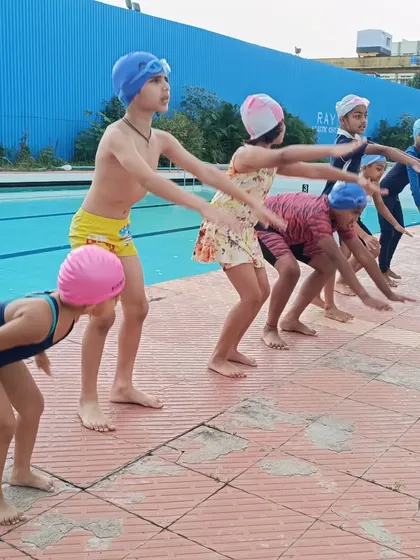 A group of beginners practicing their diving stance on the pool deck, a foundational dryland drill.