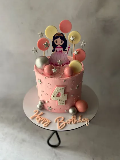 A pretty pink princess cake for a fourth birthday, decorated with edible lollipops, silver stars, and a princess topper.