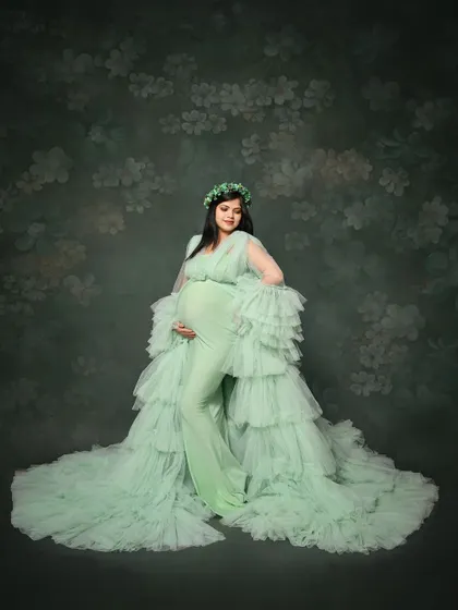A serene solo portrait of the mom-to-be in a full-length mint green ruffled gown. The soft, floral-patterned backdrop complements the dress perfectly, creating a gentle and elegant look.