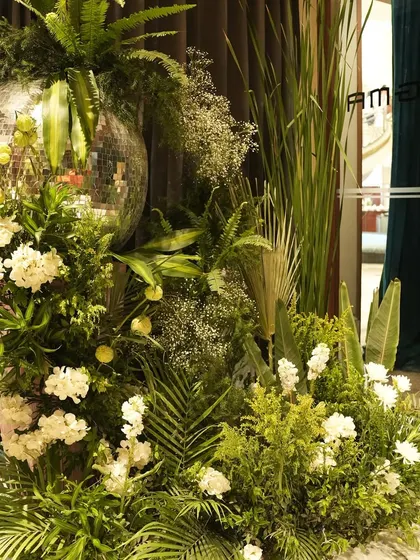 A detail shot of a floral arrangement from the jungle party, where a disco ball is nestled amongst white flowers and a variety of green leaves. This shows the creative and playful fusion of different design elements.