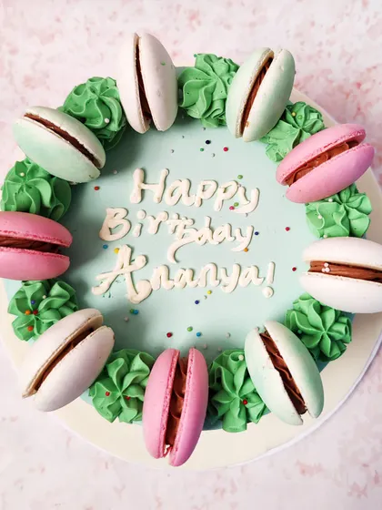 We combine two French classics in this elegant macaron cake. A ring of colorful macarons in pink, white, and mint green sits atop a pastel green cake, creating a simple, chic, and delicious design for a birthday.