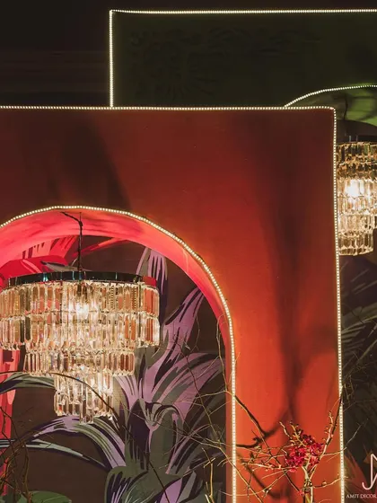 A detailed shot of the arched backdrops, where neon light outlines and hanging crystal chandeliers contrast beautifully with the bold, tropical prints.