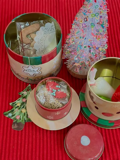 A peek inside our Christmas goodie tins. This image shows gingerbread cookies and a DIY decorating kit with sprinkles, all packed in charming, reusable Christmas-themed containers.
