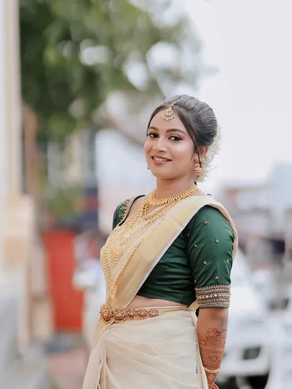 A bride in a classic Kerala kasavu saree with a green blouse. Her makeup is traditional and elegant, with gold jewellery and a simple, neat hairstyle.