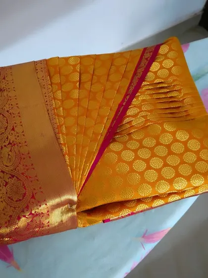 A pre-pleated mustard yellow silk saree with a red and gold border. The pleats are set and ready, making it incredibly easy for the client to drape.