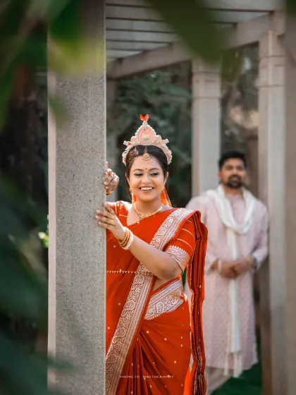 The beautiful Bengali bride, wearing the traditional 'mukut', peeks out from behind a pillar.