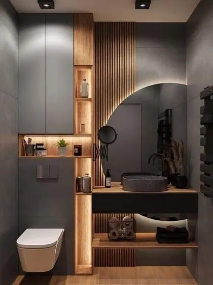 This moody and modern bathroom uses grey tones, wood accents, and clever lighting in the open shelves to create a sophisticated and cozy space.