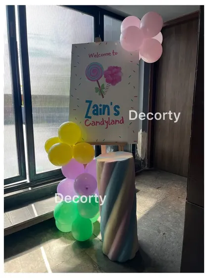 A welcome sign for 'Zain's Candyland', featuring a marshmallow-themed pedestal and colorful balloons.