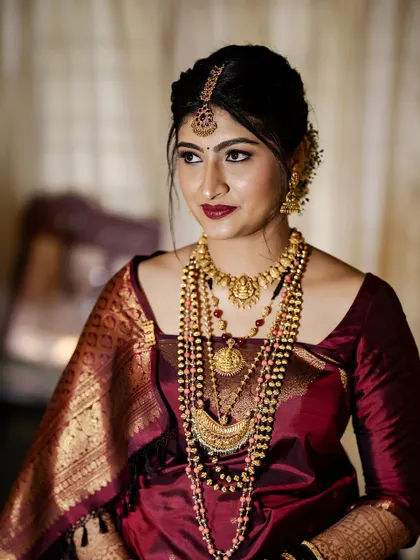 A portrait of the bride in a deep maroon saree. Her makeup is elegant and sophisticated, with a matching bold lip.