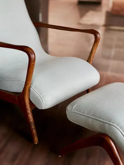 A close-up of the armrest and seat of the curved teak armchair, showing the seamless joinery and the quality of the wood finish.