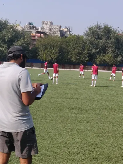 A coach observes a match with a clipboard in hand, analyzing player positioning and team shape. Constant evaluation is key to tactical improvement.