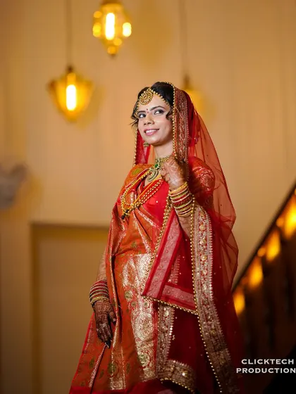 A beautiful three-quarter portrait of the bride, her smile and bright red saree lit by the warm indoor lights.