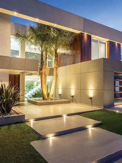 Smart landscape and exterior lighting can transform a home's entrance. Here, uplighting on the palm trees and facade walls creates a dramatic and welcoming approach, highlighting the modern architecture and biophilic elements.