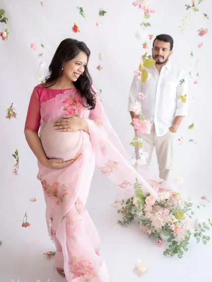 A dreamy and romantic portrait. The couple is surrounded by a shower of soft pink flowers, creating a magical atmosphere as they celebrate their growing family.