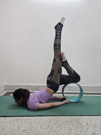 Backbend over a yoga wheel, legs reaching up while the wheel supports the spine.