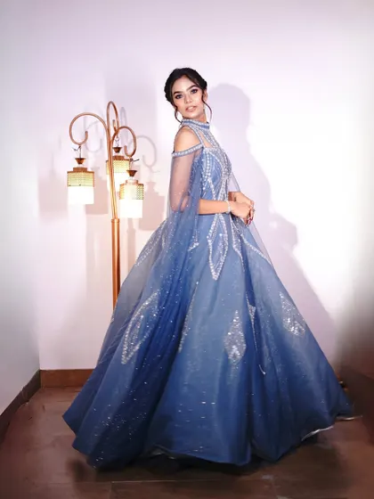 A full-length view of the blue gown, showing off the dramatic cape sleeves and the sparkling details on the skirt.