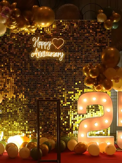 A gorgeous 25th-anniversary celebration featuring a gold shimmer wall, a 'Happy Anniversary' neon sign, large marquee numbers, and an elegant balloon arch in olive green, cream, and gold.