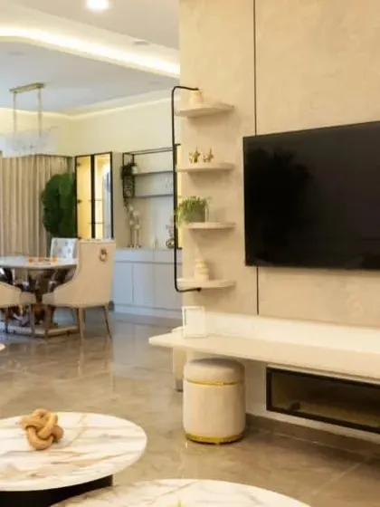 A luxurious living room from the Bren Zahara project, where a beige and marble TV unit is complemented by soft, curved wall sconces. The design creates a sophisticated and serene ambiance for relaxation.