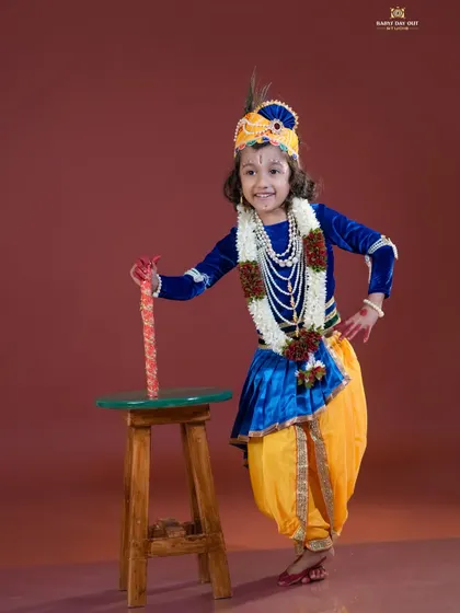 A happy little Krishna posing for his photo. The vibrant colors of the costume and background make for a stunning portrait.