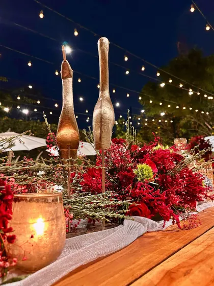A close-up of a table centerpiece from the "Scarlet Symphony" event, featuring red flowers and golden bird accents.