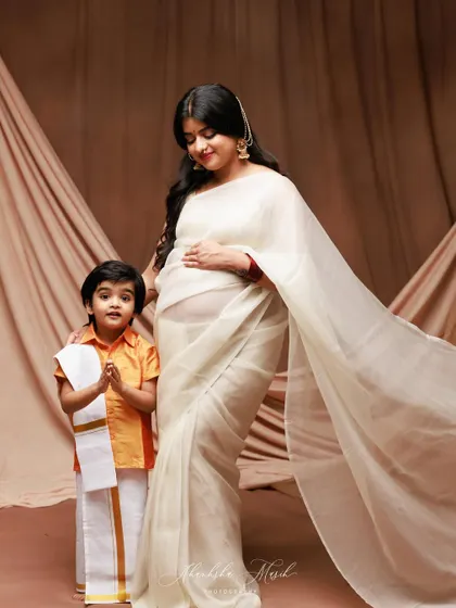 A heartwarming family portrait, with the mother-to-be in a beautiful white saree and her son in traditional dress, looking on with love.