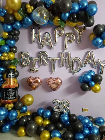 A fun and masculine theme for a 28th birthday. This decoration uses blue, black, and gold balloons, "Happy Birthday" foil letters, and includes a large whiskey bottle foil balloon for a playful touch.