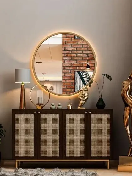 Part of a full villa interior, this console table features a dark wood cabinet with cane-front doors. The large, backlit round mirror and a golden sculpture create an elegant and welcoming vignette.