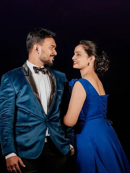 A classic couple portrait against a dark background. The focus is entirely on them and their coordinated blue outfits, showcasing the elegance of the velvet tux and gown.